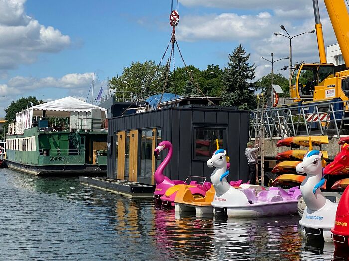 Floating tiny home being lifted near colorful paddle boats by the water