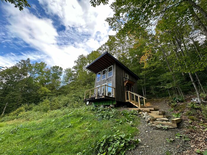 Compact wooden tiny home elevated on a hillside surrounded by green trees