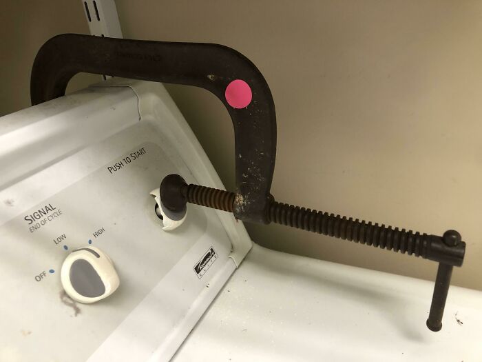 Rusty clamp securing a broken washing machine k**b in place, a technically works DIY solution to fix the problem.