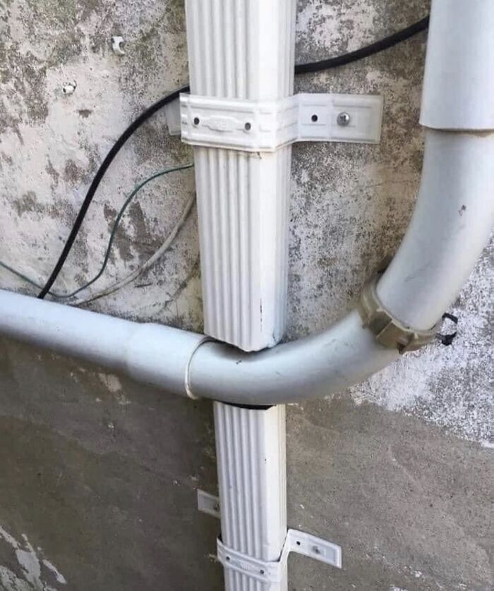 Technically works plumbing solution with a pipe awkwardly bent to fit around a vertical drainpipe against a rough exterior wall.