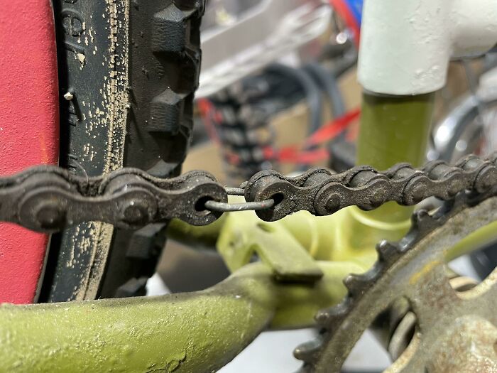 Close-up of a bike chain fixed with a bent wire, showing a technically works but hilariously dumb solution to a problem.