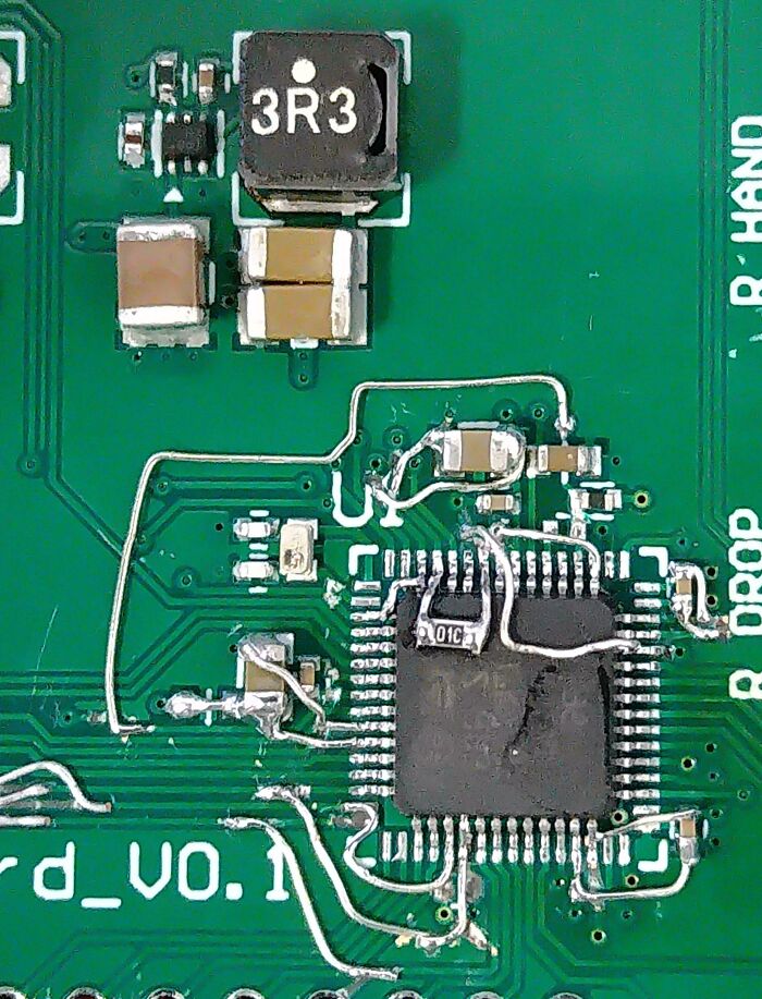 Close-up of a circuit board with a technically works fix using white patch wires soldered around a chip.