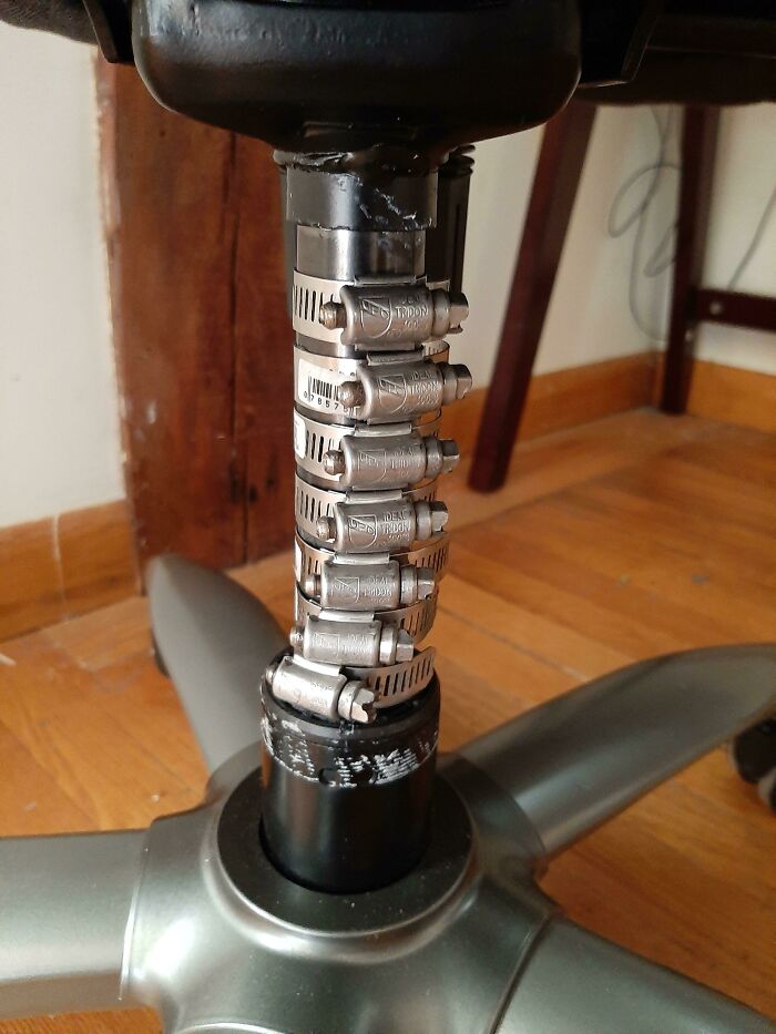 Multiple hose clamps stacked on a chair's metal base pipe as a technically works but dumb solution to fix it.