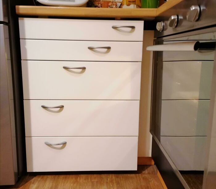 White kitchen drawers with mismatched handles and an uneven arrangement, showing a technically works solution.