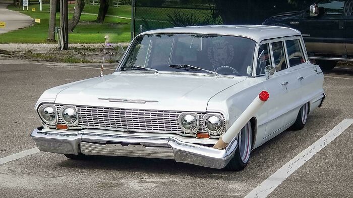 Classic white car with a creatively attached white pipe on the side, demonstrating a technically works solution.