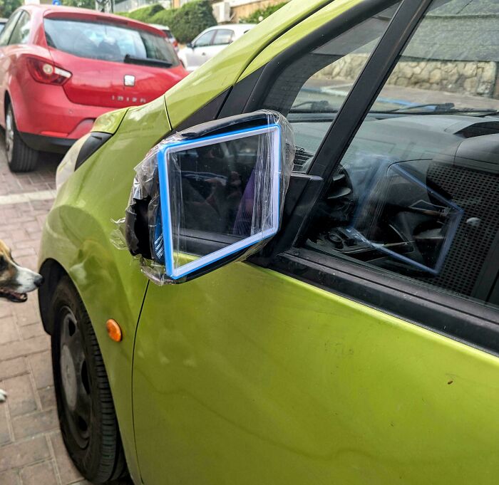 Side mirror of a green car replaced with a taped tablet as a technically works solution to a problem.