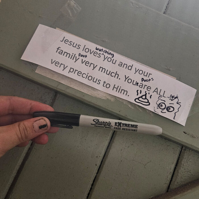 Hand holding a black Sharpie near a taped note with altered text and doodles, showing a hilariously dumb solution.