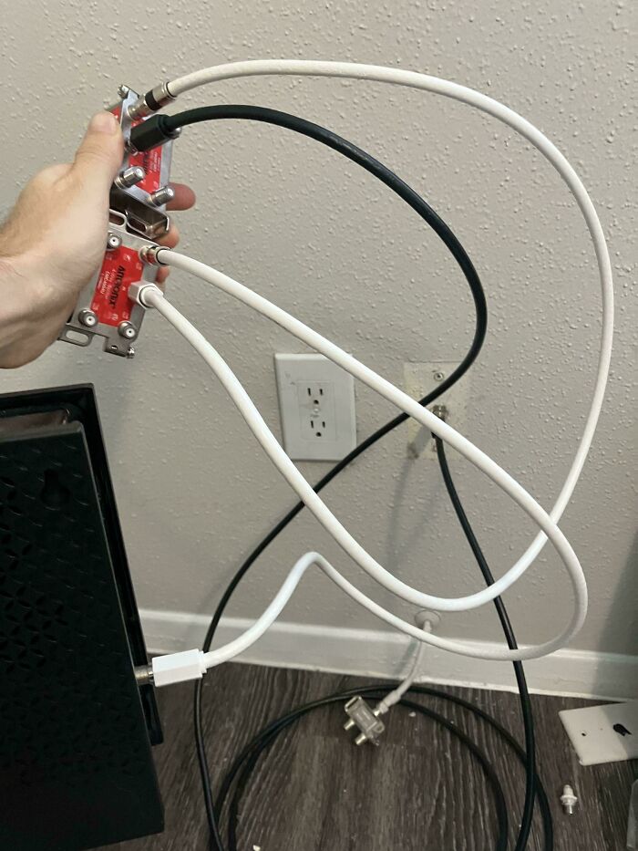 Hand holding a complicated setup of coaxial cables and splitter, showing a technically works but awkward cable solution.