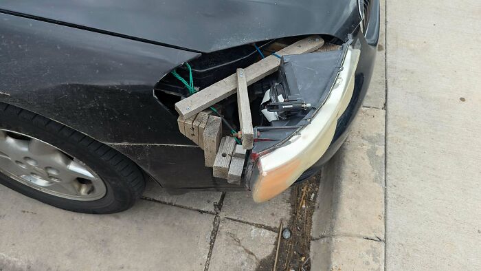 Car headlight held in place with wooden planks and wires showing a technically works but dumb solution to a problem.
