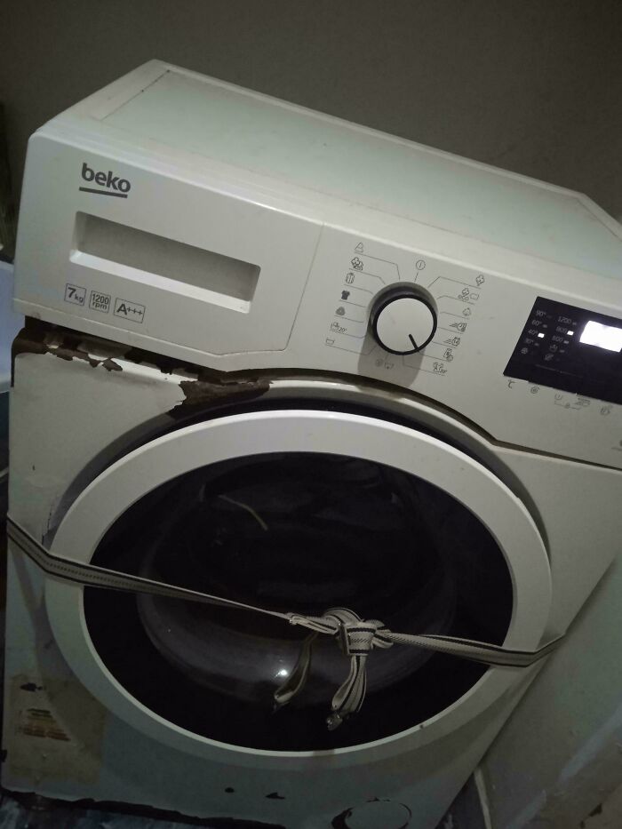 Washing machine with broken door held shut by a tied strap, a technically works but dumb solution to the problem.