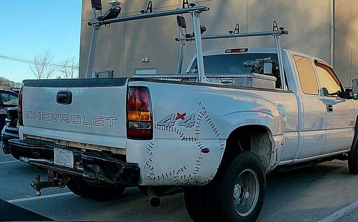 White Chevrolet pickup truck with duct tape patching a large rusted hole on the rear side, a technically works solution.