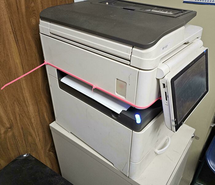Printer held together with a pink rubber band as a technically works solution to a broken or loose part.