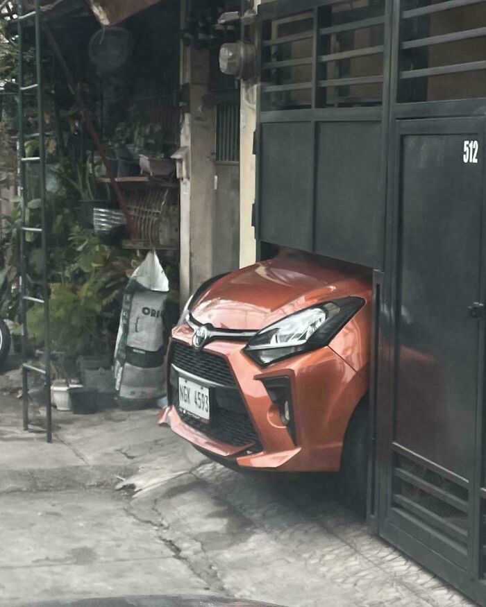 Orange car technically works by squeezing through a narrow garage entrance with the gate partially open.