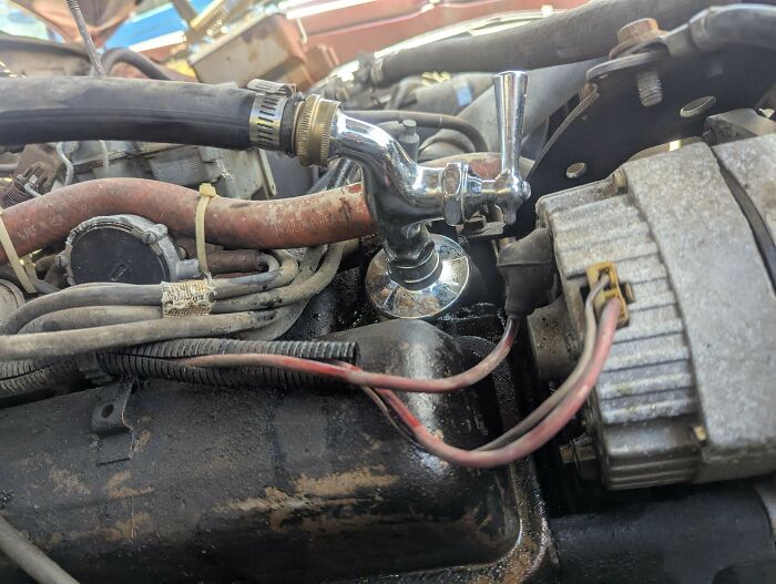 Car engine with a faucet attached to a hose as a technically works but dumb solution to a problem.
