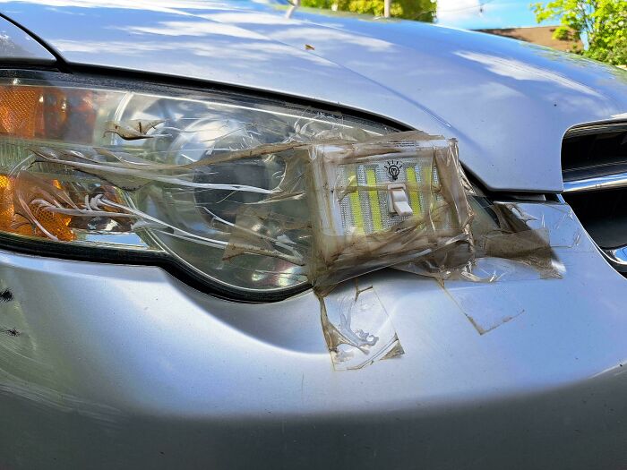 Car headlight covered with taped light switch as a hilariously dumb solution that technically works.