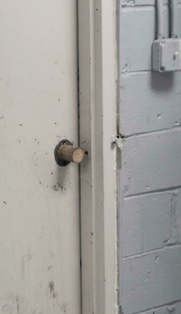 Close-up of a door with a technically works wooden k**b replacing a traditional door handle on a white metal door.