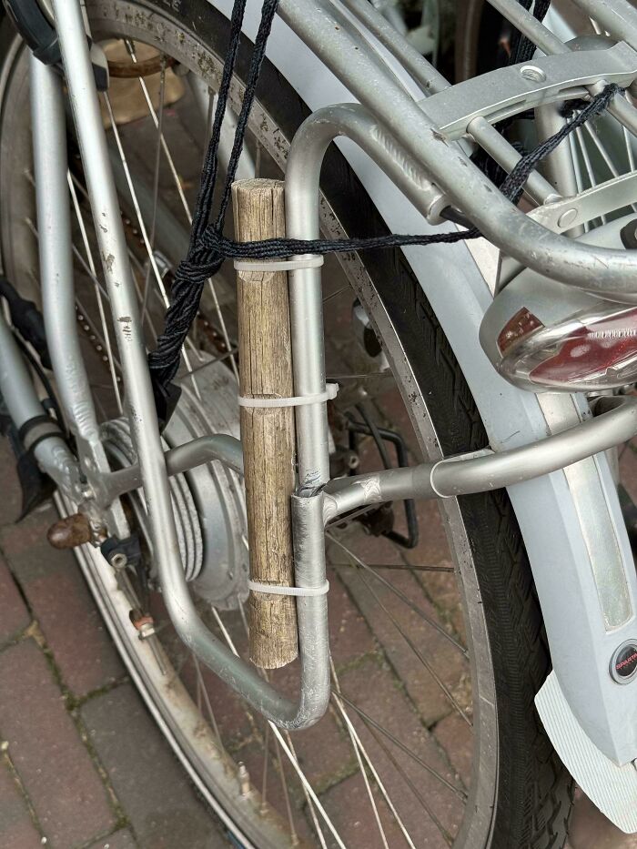 Bicycle with a wooden stick attached using zip ties and rope as a technically works solution to a problem.