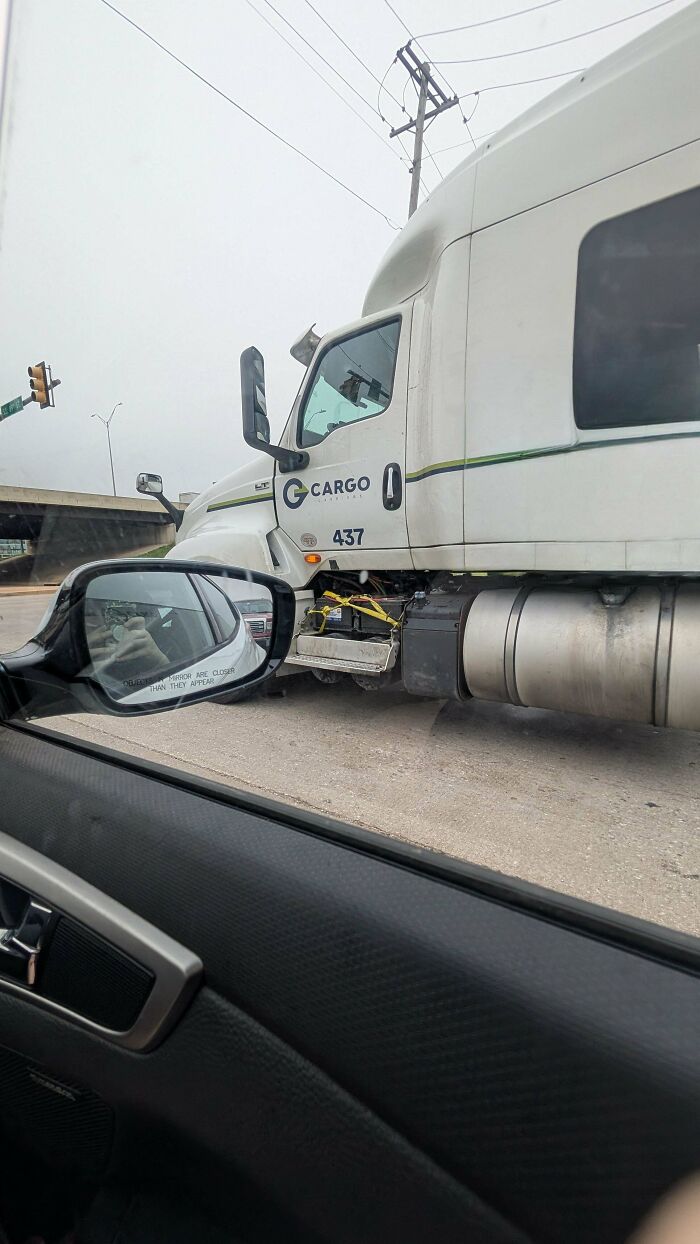 View from car window showing a truck with a hilariously dumb but technically works tie-down solution at the side step.