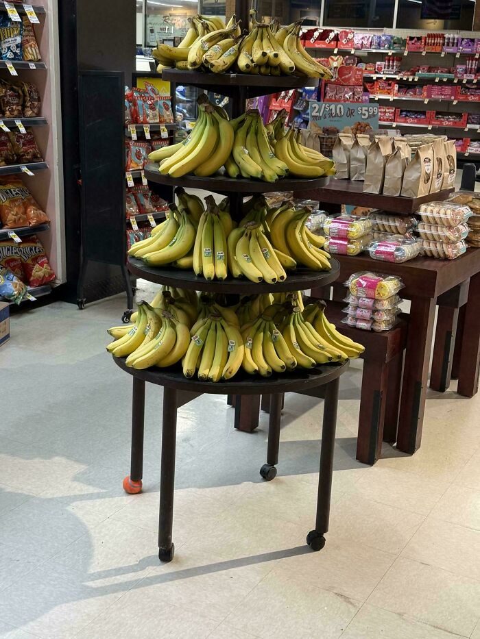 Bananas arranged on a tiered display stand with mismatched wheels in a grocery store showing a technically works fix.