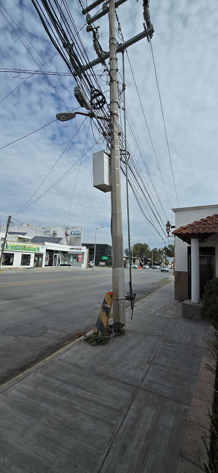 Electric pole supported by a tilted road sign post on a city sidewalk, a technically works solution to stability.