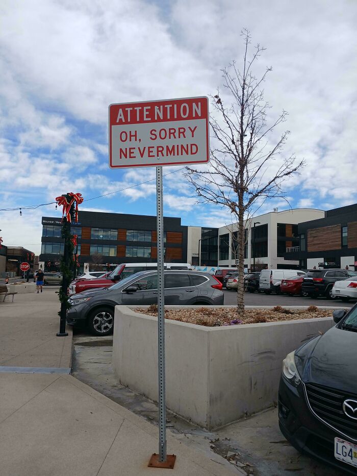 Confusing and funny street sign reading attention oh sorry nevermind in an urban parking lot scene.
