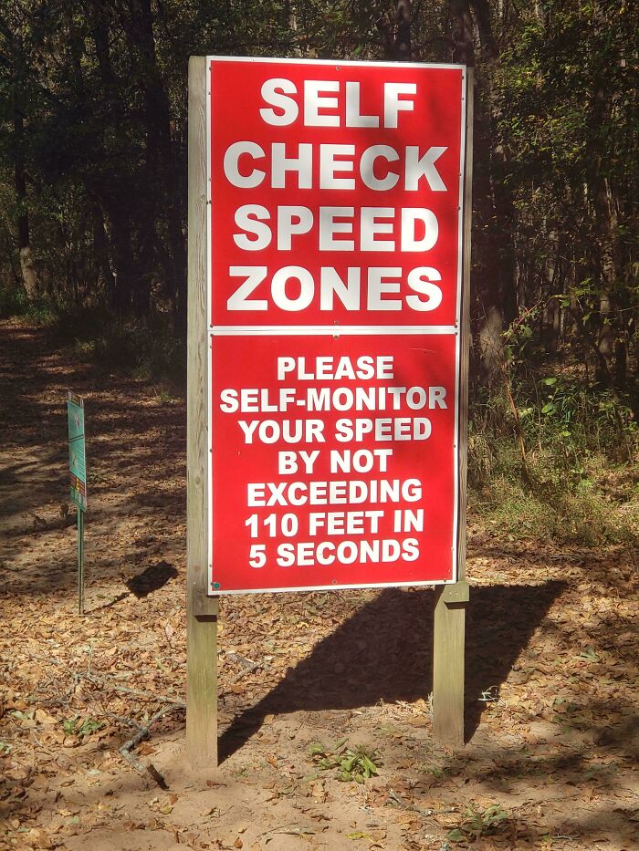 Red sign in a wooded area instructing self check speed zones and to self-monitor speed humorously.