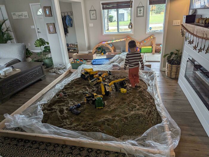 A young boy stands in an indoor sandbox with toy construction vehicles. Feel-good posts for Dads.