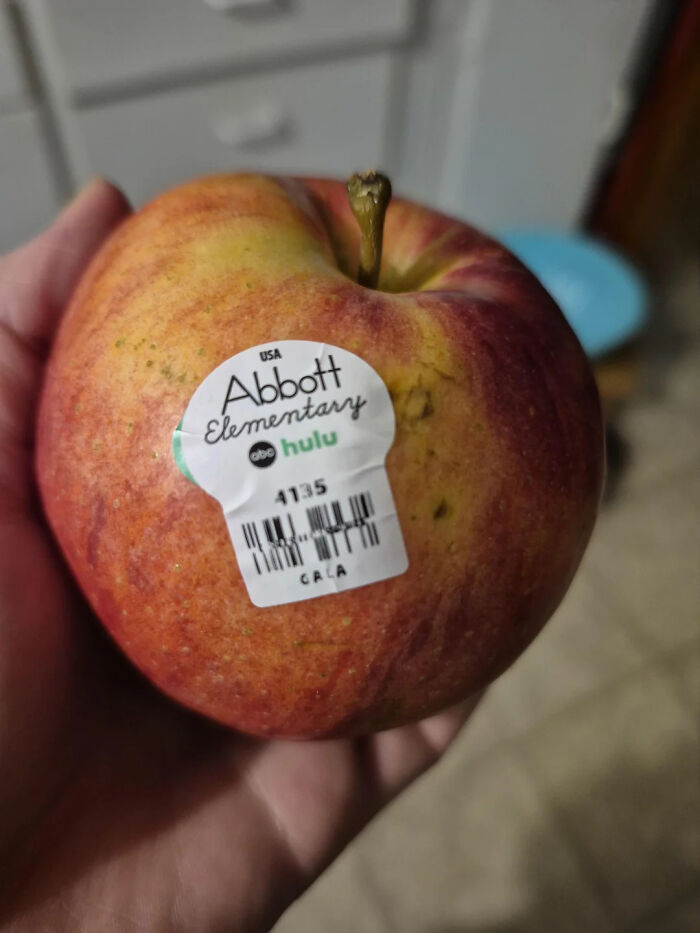 Hand holding an apple with a promotional sticker for a TV show, illustrating design that feels genuinely evil.