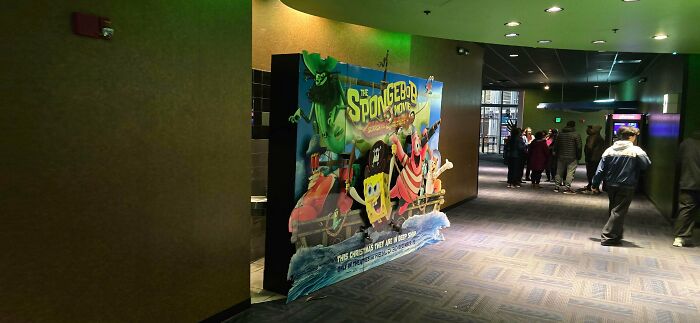 SpongeBob SquarePants movie advertisement in a dim hallway with people walking past, showing design that feels genuinely evil.