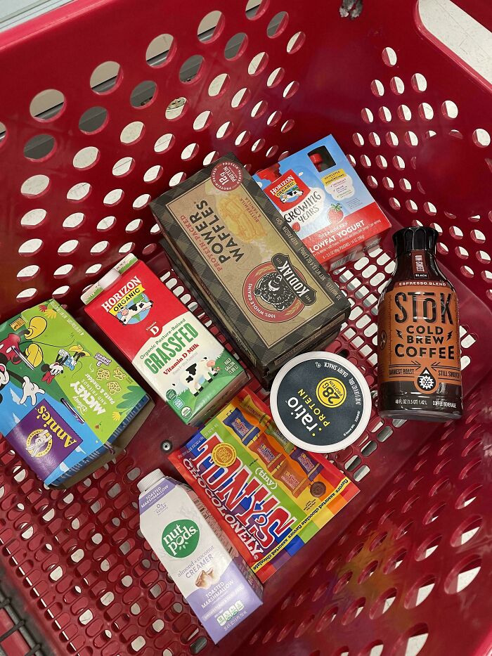 Grocery items including coffee, yogurt, waffles, milk, candy, and creamers in a red shopping cart showing grocery costs.
