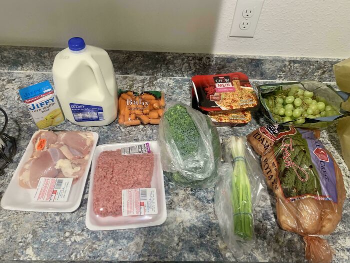 Assortment of groceries including meat, milk, vegetables, and packaged noodles showing grocery costs where they live.