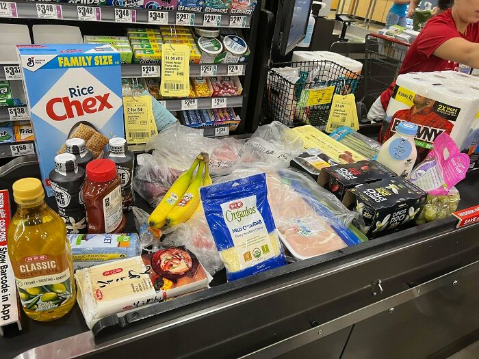 Groceries on a supermarket conveyor belt showing prices and variety, illustrating how much groceries cost where they live.