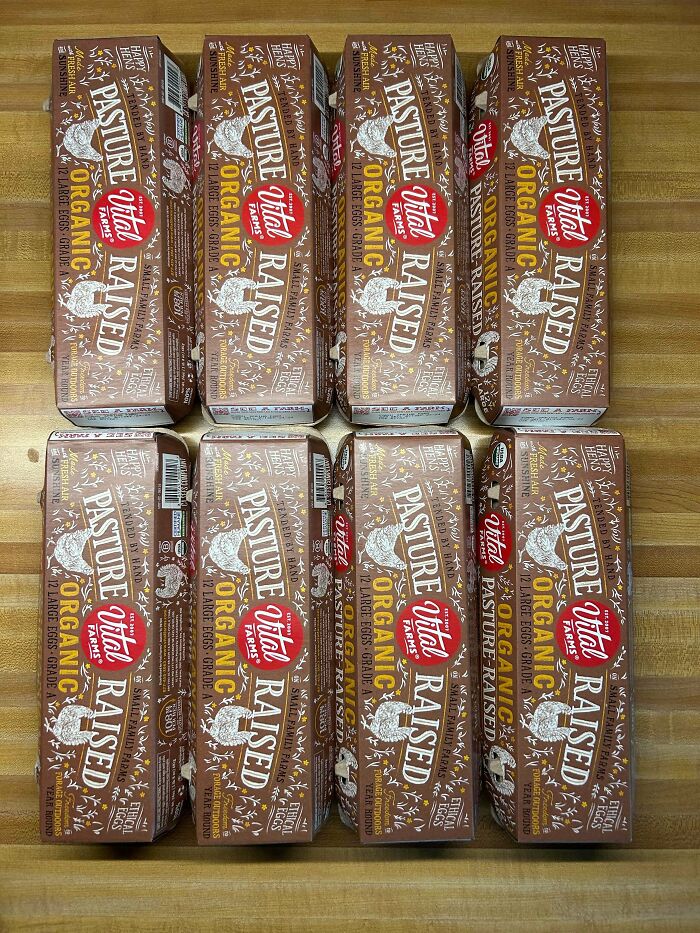 Eight cartons of organic pasture-raised eggs on a wooden surface showing grocery costs where they live.