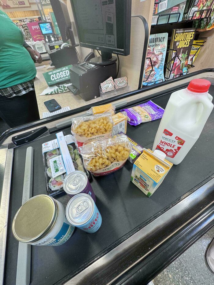 Grocery items including milk, pasta, drinks, and sushi on a checkout conveyor belt showing grocery cost where they live.