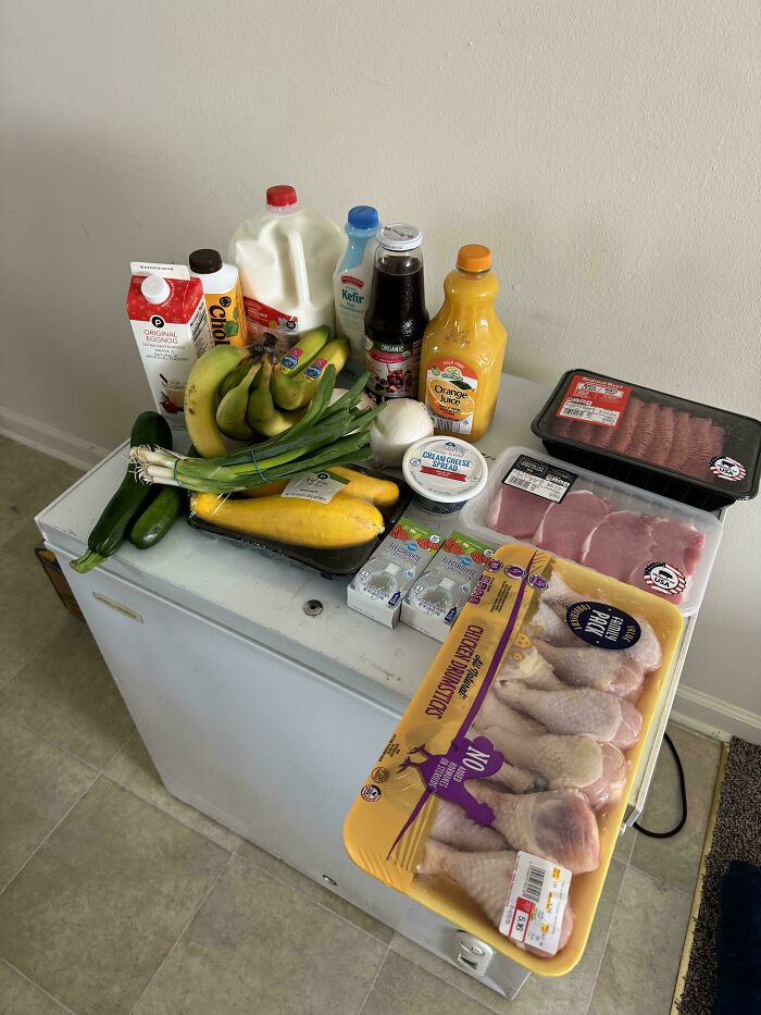 Groceries including milk, bananas, meat, and juice displayed on a white freezer showing grocery cost comparison.