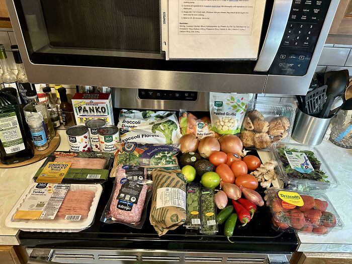Assortment of groceries including fresh produce, meat, and pantry items displayed on a kitchen counter showing grocery costs.