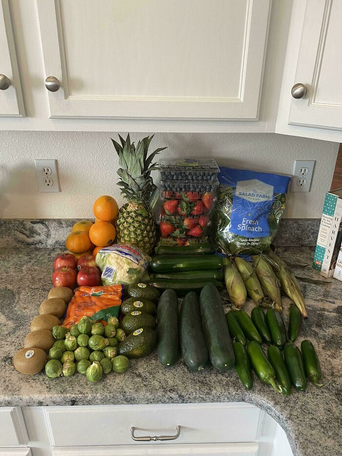 Assortment of fresh groceries including fruits and vegetables displayed on kitchen counter showing grocery costs.