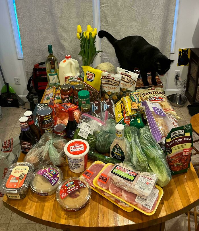 A variety of groceries including fresh produce, packaged foods, and beverages on a table showing grocery cost where they live.