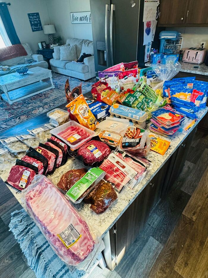 Large grocery haul displayed on a kitchen counter showing the cost of groceries where people live with various meats and snacks.