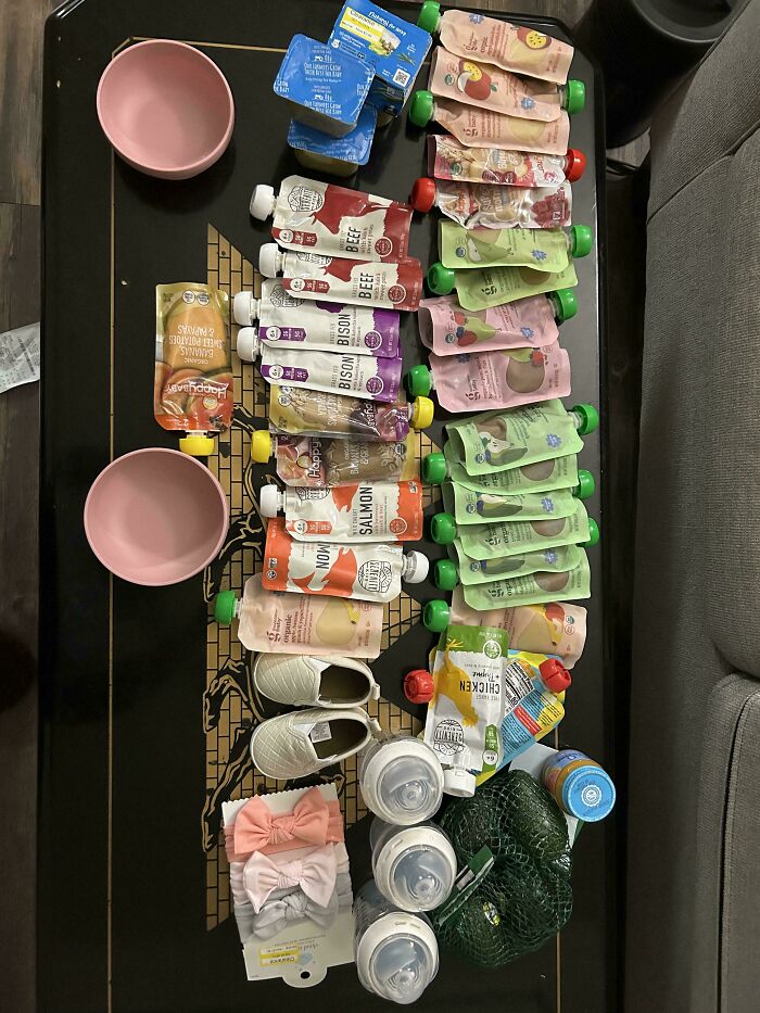 Various baby food pouches, bottles, shoes, and groceries laid out showing how much groceries cost where they live.