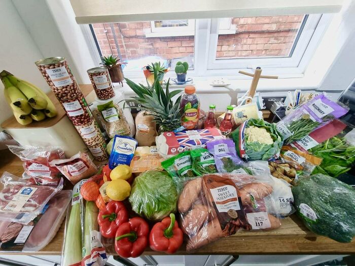 A variety of groceries including fresh produce, canned goods, and packaged items displayed on a kitchen counter showing grocery costs.