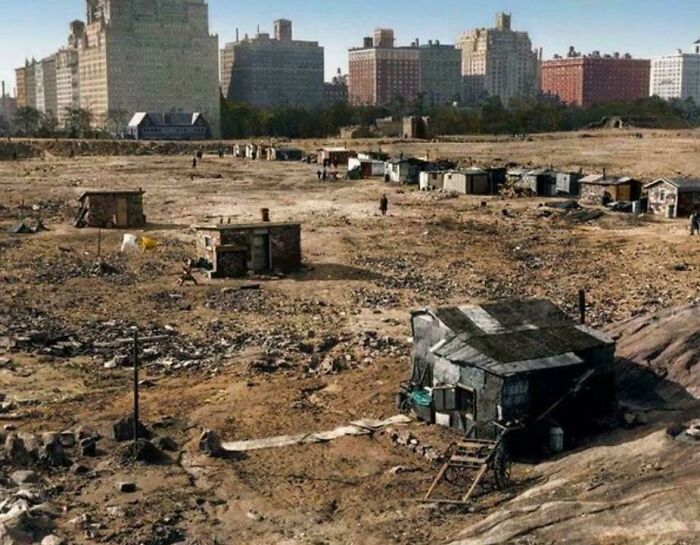 Shanties in a desolate field with large buildings in the background, an interesting photo of contrast.