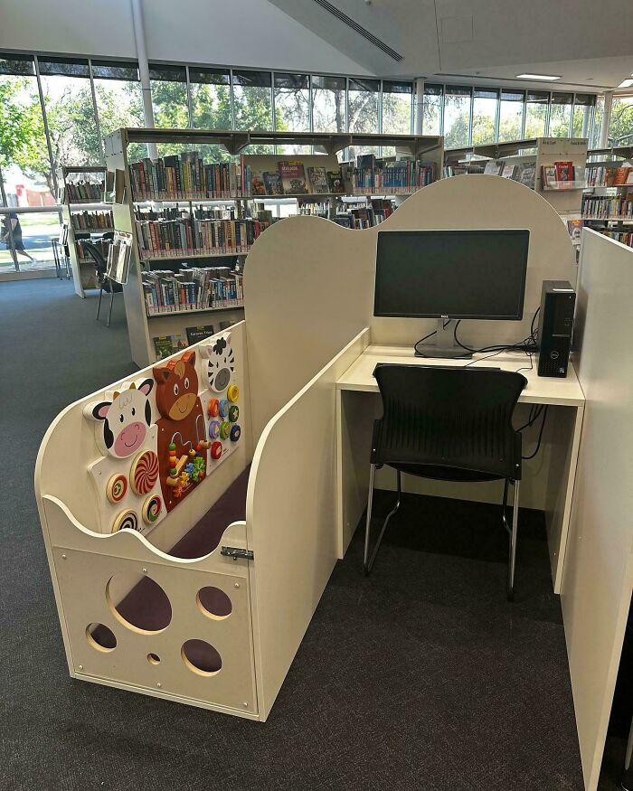 A unique library workstation with a toddler playpen beside the desk, an interesting photo.