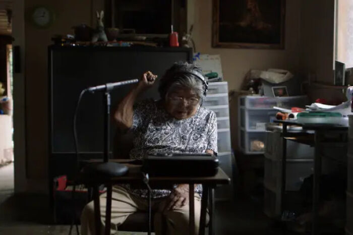 An elderly woman wearing headphones and speaking into a microphone, an interesting photo of a unique activity.