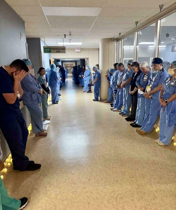 Medical staff lined up in a hospital hallway, heads bowed in what appears to be a moment of reflection, a d**n interesting and poignant photo.