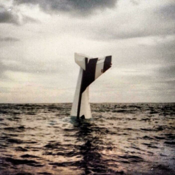 An interesting photo of a partially submerged white and black striped object in the ocean under a cloudy sky.