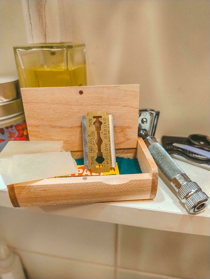 A close-up of a double-edge razor blade in a wooden box, next to a safety razor. Frugal tips for personal care.