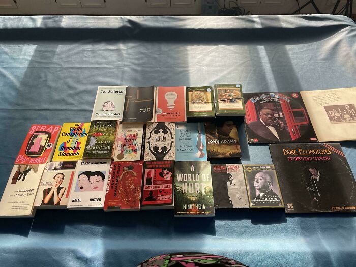 A collection of books, DVDs, and records laid out on a light blue fabric, offering frugal tips for a new world.