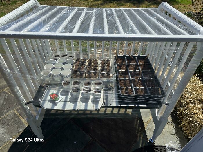A repurposed white crib, covered with plastic, functions as a cold frame for growing seedlings, a frugal tip for a new world.