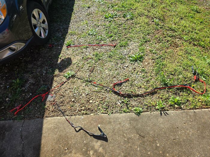Jumper cables on grass and concrete near a car tire, illustrating practical tips for this economy.